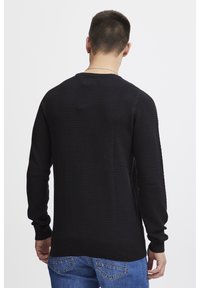 Pulover negru tricotat cu un model texturat, cu mansete și tiv ondulat. Purtați peste blugi albaștri, arătând un design simplu și clasic din spate.