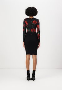 Jupe noire côtelée avec une silhouette ajustée, associée à une chemise à manches longues arborant un motif de roses rouges. Portée avec des chaussures noires et des chaussettes.