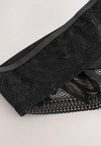 Sous-vêtements en dentelle noire avec motifs floraux et détails en mesh sur un fond clair.