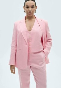 Pink linen suit featuring a double-breasted blazer with flap pockets and a matching vest with buttons, paired with tailored trousers.