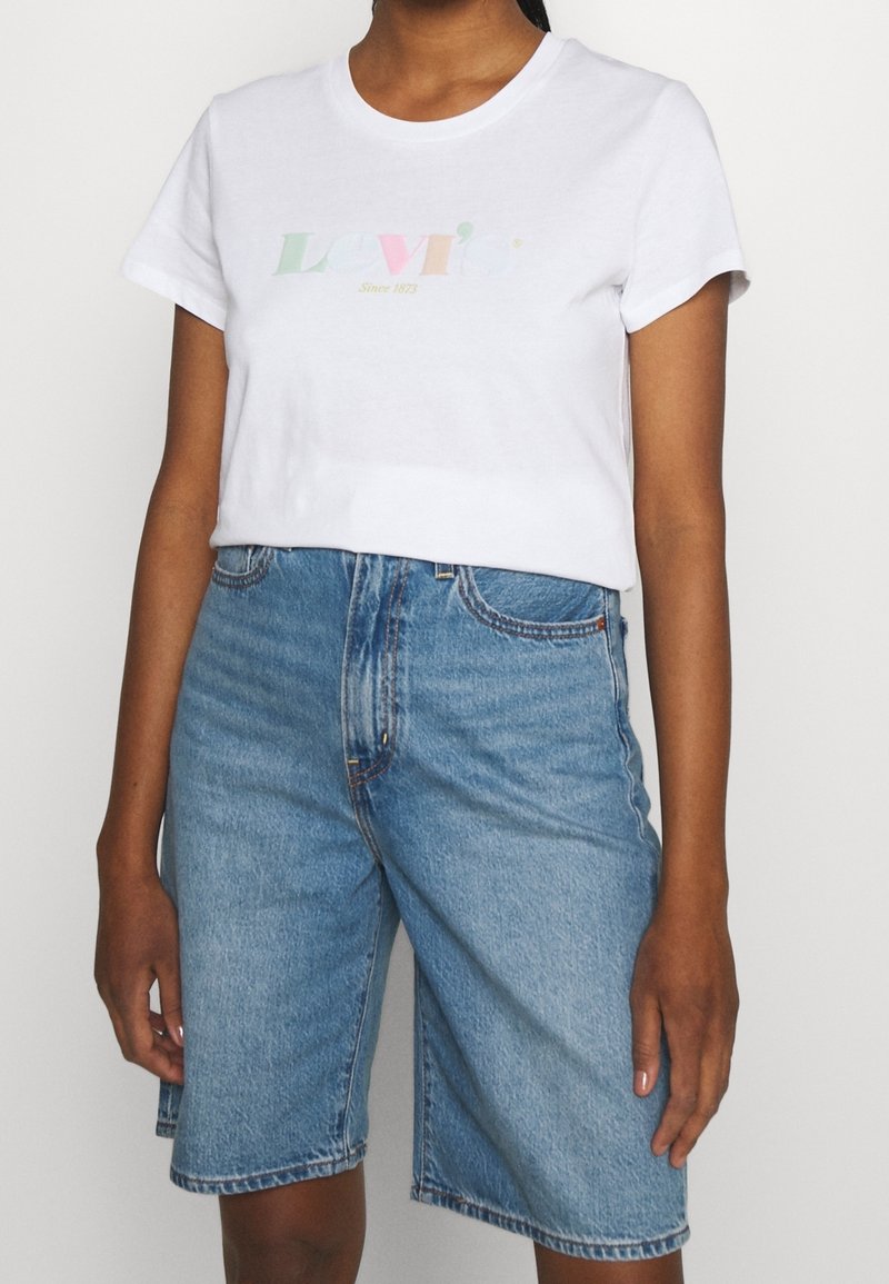 Valkoinen lyhythihainen t-paita, jossa on pastellinvärinen Levi's-logo ja teksti "Since 1873", yhdistettynä vaaleansinihin farku shortsien kanssa, joissa on käänteet.