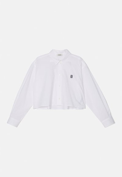White cropped button-up shirt with long sleeves, featuring a classic collar and a small black embroidered logo on the left chest.