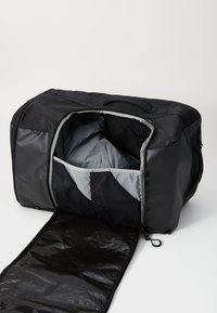 Svart duffelbag med grå innside, glidelåsåpning, nettinglomme og avtakbar svart bunn. Laget av slitesterkt stoff, rektangulær form.