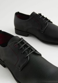 Zwarte veterschoenen met een gestructureerde afwerking, voorzien van glad leer en een subtiele rode accent in de stiksels en de veterogen.