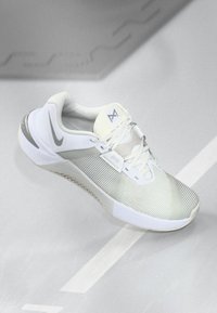 White athletic shoe with a textured mesh upper, lace-up closure, and rubber sole. Features subtle gray accents and a prominent logo.