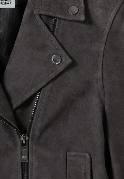 Giubbotto da motociclista in suede grigio con chiusura a zip, bottoni a scatto e risvolti angolati, caratterizzato da una texture liscia e dettagli di cucitura visibili.
