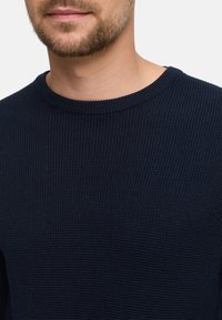 Marineblauer Strickpullover mit einem strukturierten, gerippten Muster und einem klassischen Rundhalsausschnitt. Nahaufnahme des Materials und der Passform.