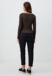 Aangesloten bruine long-sleeve top met ribbeltextuur en wijde halslijn, gecombineerd met zwarte tapered broek en zwarte sneakers.