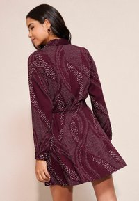 Burgunderfarbendes bedrucktes Kleid mit einem kragenlosen Ausschnitt, langen Ärmeln, einer taillierten Taille und abstrakten weißen Punktmustern. Weicher Stoff mit fließendem Sitz.