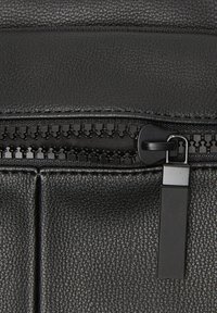 Pochette nera in pelle ecologica testurizzata con una cerniera liscia dotata di un tirante nero e dettagli. Le cuciture sono visibili lungo i bordi.