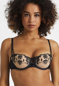 Soutien-gorge en dentelle noire avec panneau beige transparent, broderie florale, soutien-gorge à armature et nœud décoratif au centre, avec bretelles réglables.