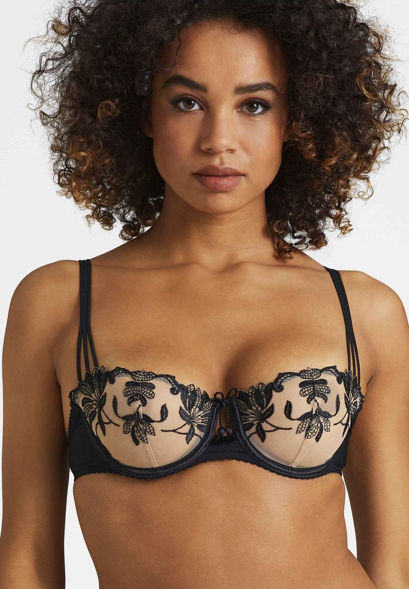 Soutien-gorge en dentelle noire avec panneau beige transparent, broderie florale, soutien-gorge à armature et nœud décoratif au centre, avec bretelles réglables.