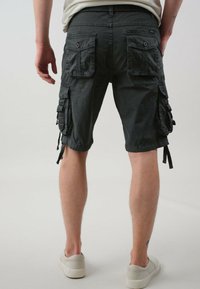 Donkergrijze cargoshorts met zij- en achterzakken, losse pasvorm, koordaccenten en zachte stof. Knieën en een deel van de onderbenen zichtbaar.