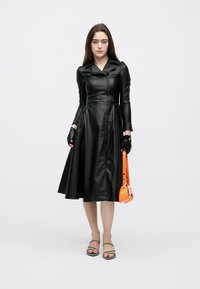 Črna usnjena obleka s tesno prilegajočim se zgornjim delom in razširjenim krilom, z ostrim ovratnikom, dolgimi rokavi in sprednjo zadrgo. Oranžna torbica in rokavice.