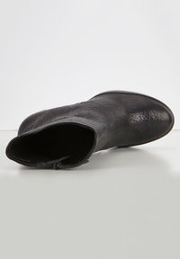 Stivale ankle in pelle nera con finitura testurizzata, punta tonda e interno liscio. È posizionato piatto su una superficie neutra, mostrando la vista dall'alto.
