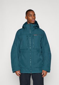 Veste imperméable bleu sarcelle avec capuche, dotée de deux poches avant zippées, de poignets ajustables et d'un détail de logo sur la poitrine.