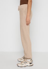 Beige knit sweatpants with textured pattern, elastic waistband, and drawstring. Paired with beige and white athletic sneakers.