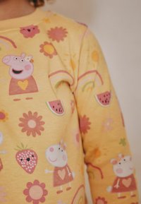 Keltainen huppari, jossa on sarjakuvamotiiveja: Peppa Possu, kukkia, sateenkaaria ja vesimeloneja. Pehmeä materiaali ja eloisat painetut kuviot.