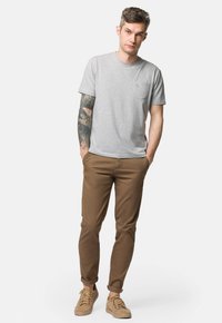 Szara koszulka z krótkim rękawem z kieszonką na piersi, zestawiona z brązowymi spodniami slim-fit i beżowymi sneakersami. Gładki materiał o casualowym designie.