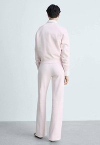 Ljust rosa lounge-set bestående av en figursydd tröja och utsvängda byxor, tillverkat av mjukt tyg med ribbade muddar och en slät textur.