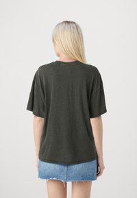 Camiseta oversized de color verde oscuro con mangas cortas, con cuello redondo y un tejido suave y texturizado. Combinada con una mini falda de mezclilla clara.