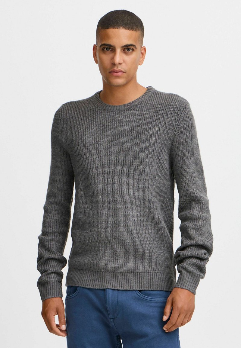 Pull en tricot côtelé gris avec des manches longues et un col rond. Présente une surface texturée et une taille ajustée.