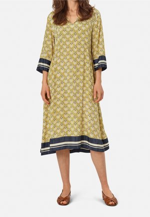 Żółta sukienka w wzory z dekoltem w serek i rękawami do łokcia. Ma ciemnoniebieski dół z białymi paskami i luźny fason.