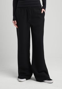 Black, wide-leg sweatpants with an elastic waistband and drawstring. Feature side pockets and a smooth, soft texture. Casual style.