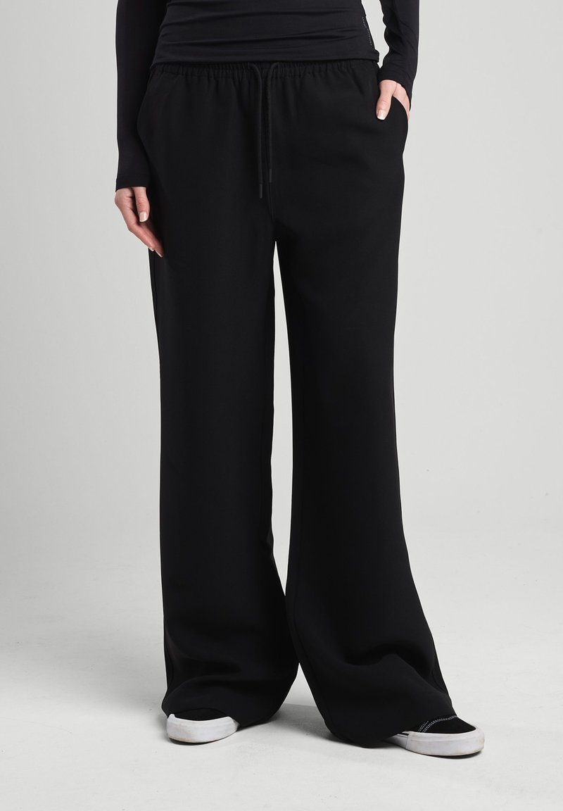 Black, wide-leg sweatpants with an elastic waistband and drawstring. Feature side pockets and a smooth, soft texture. Casual style.