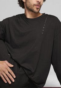 Schwarzes Langarmshirt aus glattem Stoff, mit einem dezenten Logo in Weiß. Das Design zeichnet sich durch eine lockere Passform und einen runden Halsausschnitt aus.