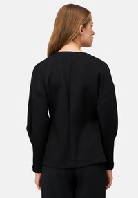 Czarna bluza dresowa o luźnym kroju, z okrągłym dekoltem, długimi rękawami i szwem z tyłu; wykonana z miękkiej, teksturowanej tkaniny.