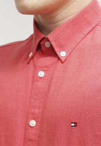 Rote Button-Down-Hemd aus strukturiertem Stoff. Verfügt über einen klassischen Kragen und weiße Knöpfe. Enthält ein kleines gesticktes Logo auf der Brust.