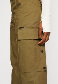 Olivově zelené cargo kalhoty s texturovaným povrchem, mají boční kapsu, zapínání na knoflík a malou černou etiketu G-Star na kyčli.