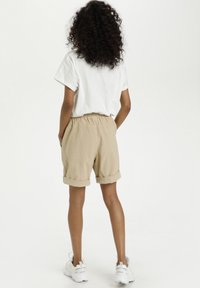 Short beige avec une ceinture élastique, revers retroussés, associé à un t-shirt blanc et des baskets blanches. Matière en coton texturée.