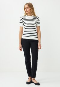 Gestreepte gebreide top in wit en zwart, korte mouwen, ronde halslijn. Gecombineerd met zwarte slim-fit broek en zwarte platte schoenen. Eenvoudig, klassiek ontwerp.