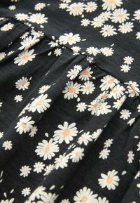 Tissu noir avec des fleurs de marguerite blanches aux centres orange clair, présenté avec des plis froncés.