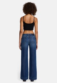 Weite blaue Jeans aus Denim mit hoher Taille, mit Gesäßtaschen und sauberen Abschlüssen. Kombiniert mit einem enger geschnittenen schwarzen Cropped-Top.