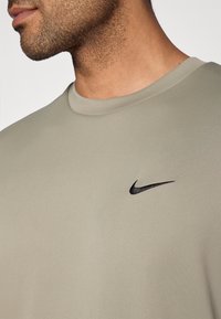 Licht olijfgroen Nike T-shirt met een ronde halslijn en een zwart logo-accent. Soepele textuur en nauwsluitend ontwerp, met minimale details.