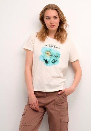 Creme kortærmet T-shirt med et turkist blomsterprint og teksten "DEN VENLIGHEDENS NATUR SJÆL." Båret med brune cargo bukser.