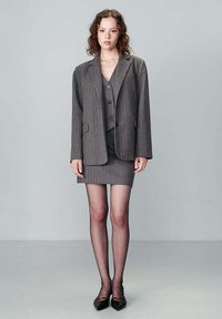 Blazer grigio a righe con un gilet coordinato e una mini gonna. L'outfit presenta linee sartoriali e una texture morbida, completato da scarpe basse.