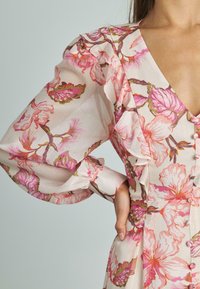 Vestido rosa claro con un patrón floral que presenta grandes flores rosas y verdes. Tiene mangas abullonadas y un escote en V con botones.