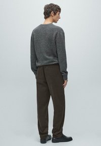 Maglione grigio in lana con scollo rotondo, abbinato a pantaloni in velluto a coste marroni. L'outfit presenta una vestibilità rilassata e dettagli di cuciture visibili.