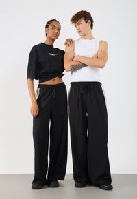 Melnas platās bikses ar auklu jostasvietā. Saskaņotas ar īsu melnu t-kreklu un baltu bezpiedurkņu topu. Gluda auduma tekstūra.