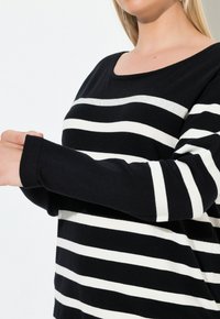 Sweter w czarno-białe paski z okrągłym dekoltem i długimi rękawami, wyróżniający się miękką teksturą dzianiny oraz różnymi szerokościami pasków.