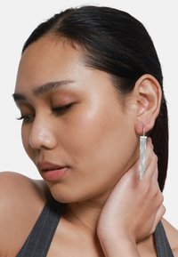 Orecchini pendenti argentati con più fili verticali. Il design presenta una forma elegante e moderna, con una finitura metallica lucida.
