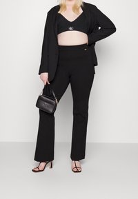 Musta bleiseri mustan braletin päällä, yhdessä tiukkojen mustien housujen kanssa. Asusteina on pieni musta käsilaukku ja remmisandaalit mustina.