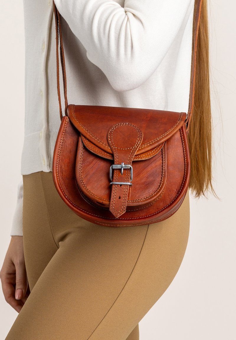 Kožená crossbody taška v gaštanovej farbe, s okrúhlym klopom, prackovým zapínaním a kontrastným šitím. Hladká textúra s nastaviteľným popruhom.