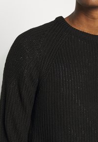 Černý pletený svetr s texturovaným vzorem, žebrovaným výstřihem a volnými rukávy, vyrobený z měkké, husté látky.