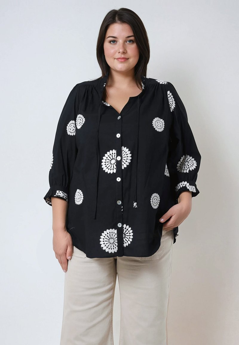 Black blouse with white floral embroidery, buttons at front, rounded neckline, and three-quarter sleeves. Fabric appears lightweight and textured.
