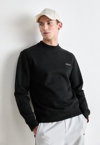 Black cotton sweatshirt with crew neckline, ribbed cuffs, and hem. Features embroidered "BOSS" logo in purple on left chest. Worn with beige cap.
